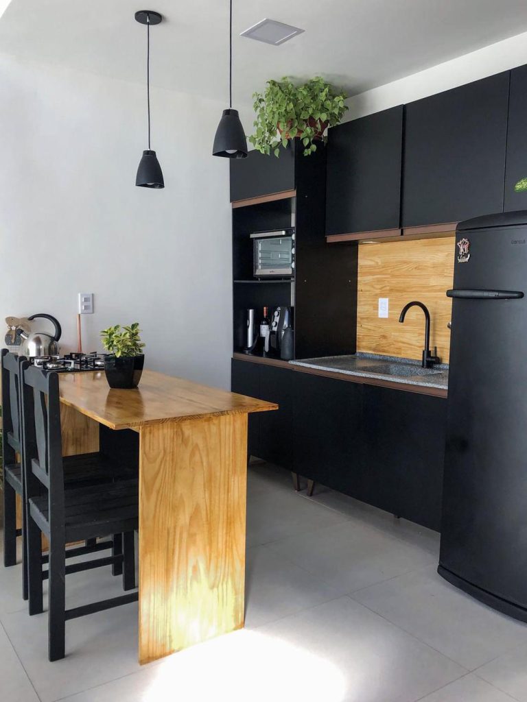 Cozinha decorada com plantas de cliente Madesa. As paredes e o piso são brancos, enquanto os móveis e eletrodomésticos são pretos e possuem detalhes em madeira.