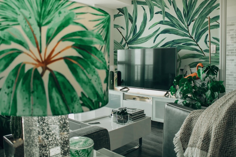 Sala de estar com papel de parede com estampa de plantas e um abajur, também estampado com a imagem de plantas.