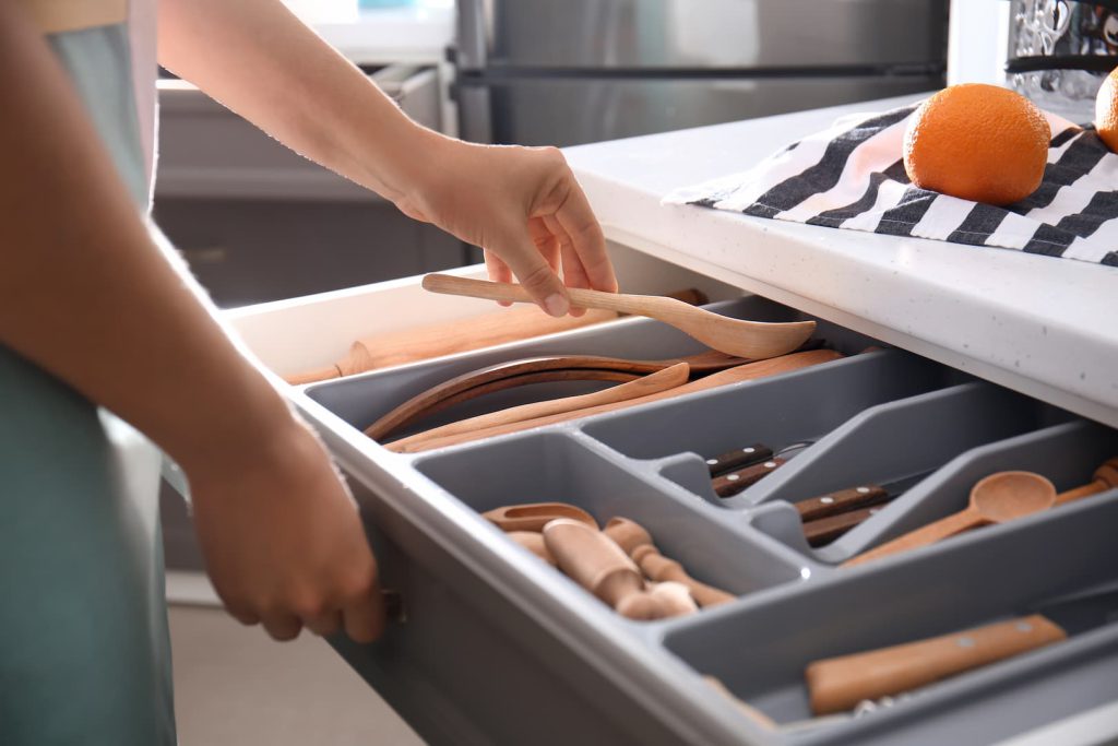Pessoa abrindo uma gaveta de talheres e utensílios organizados em divisórias, uma excelente dica para ter uma cozinha funcional.