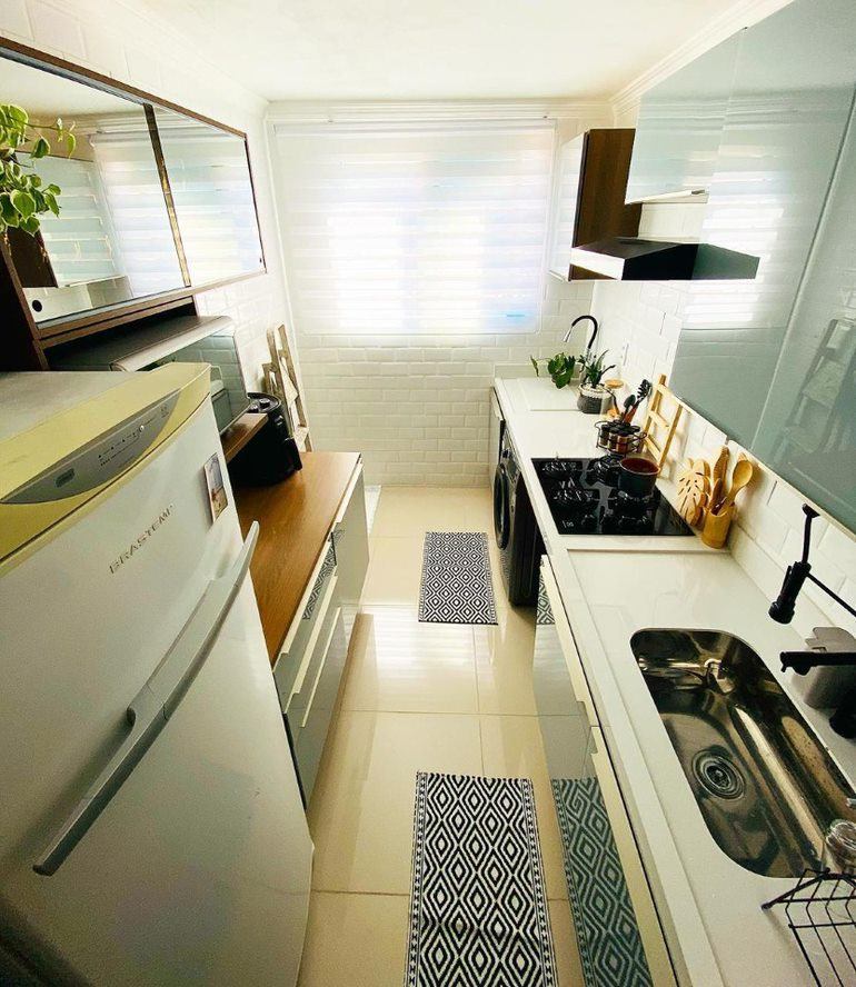 A imagem ilustra uma cozinha vista de cima com uma geladeira, armários e uma bancada com pia, representando as opções de presente para casa nova.