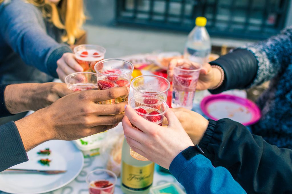 Mãos de pessoas brindando com bebidas de frutas, exemplificando o encontro de amigos em um home bar.