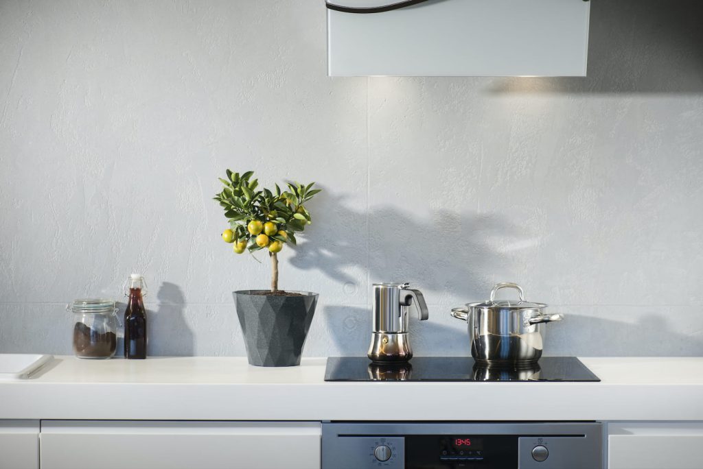Cozinha toda branca com alguns utensílios em inox e um vaso de planta para exemplificar uma cozinha minimalista.