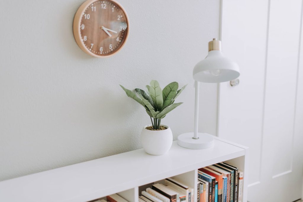 Imagem de uma prateleira de livros brancas decorada como um abajur e um vaso de plantas, itens decorativos que combinam com o minimalismo.