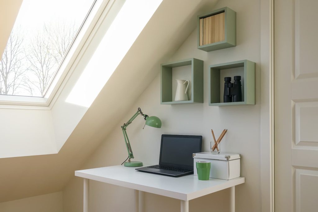 Home office com entrada de iluminação natural, escrivaninha branca e nichos verdes.