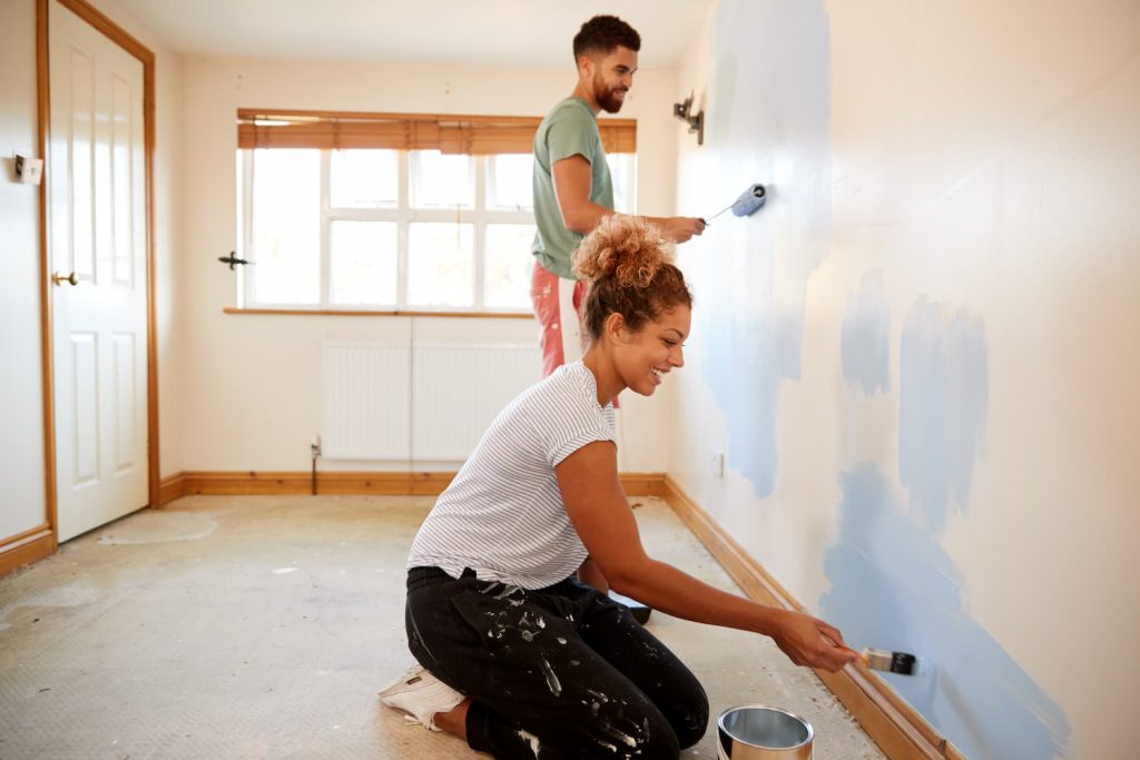Casal pintando uma parede branca de azul em uma casa que está sendo reformada.