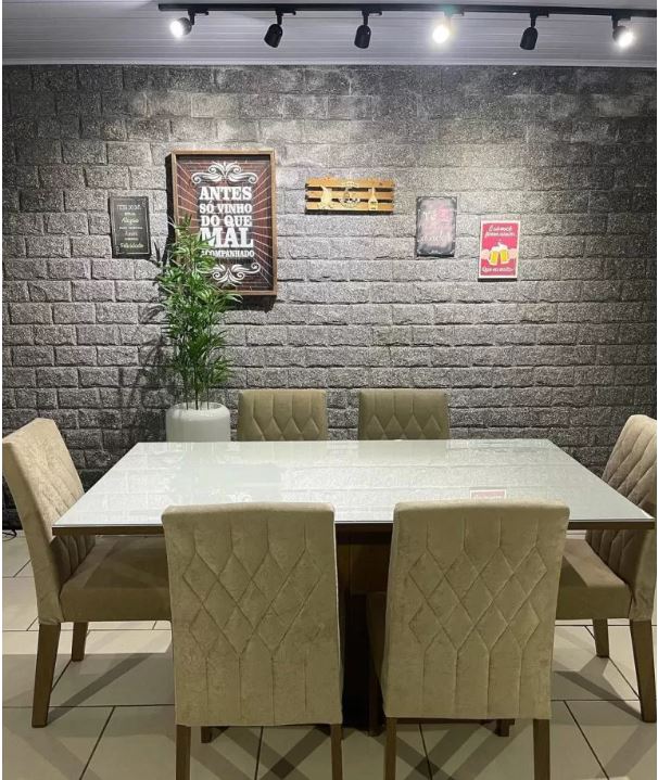 A imagem mostra como montar uma sala de estar moderna, mostrando uma mesa grande com um fundo decorado com quadros em uma parede de tijolos cinza.