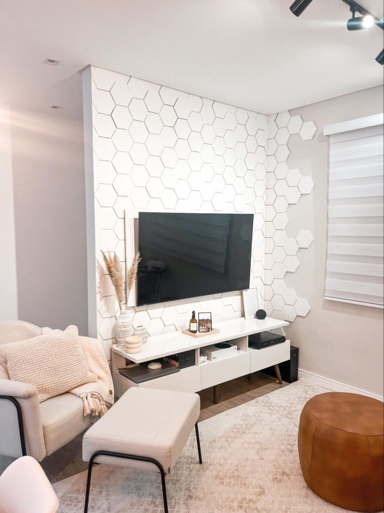 A imagem mostra uma sala de estar moderna, com sofás brancos grandes, luzes e uma tv.