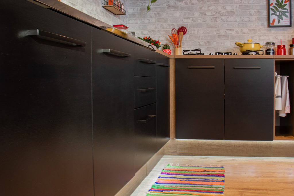 A imagem ilustra um dos tipos de cozinha com bancada Madesa, na cor preta. Em cima estão diferentes acessórios, como uma panela amarela e utensílios vermelhos.