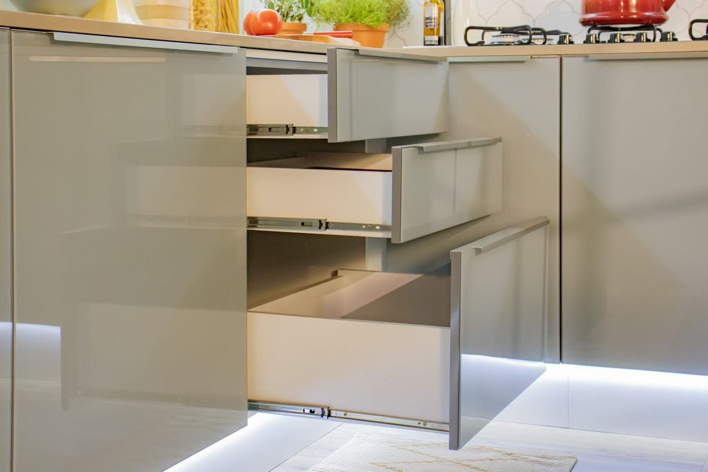 A imagem ilustra um estlo de cozinha delicado, de cor clara, com bancada e várias gavetas abertas.