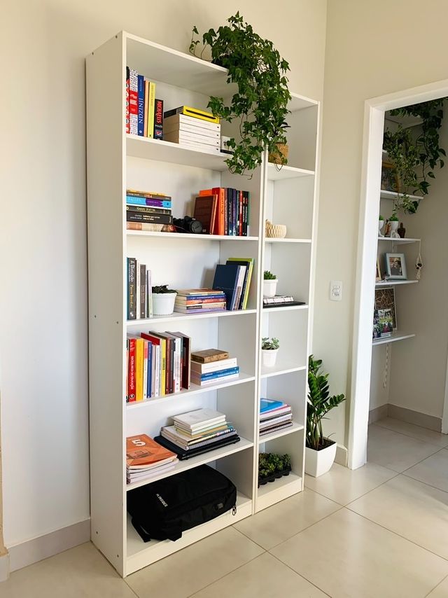 A imagem ilustra uma estante branca com livros e plantas como ideias para trabalhar em casa de forma organizada.