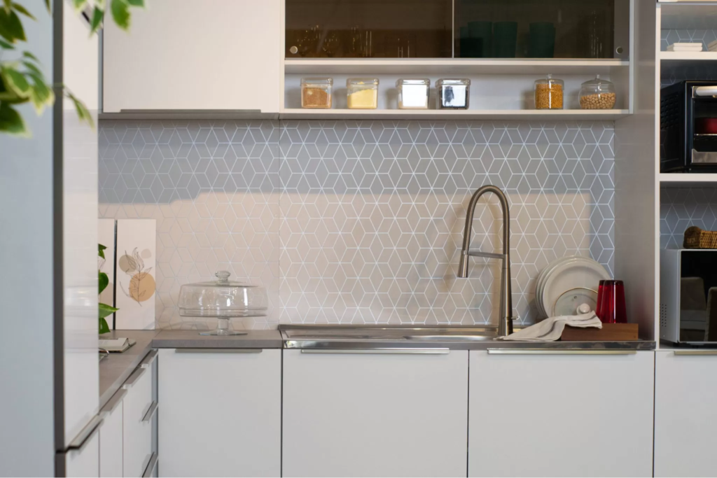 A imagem ilustra uma cozinha planejada branca, com armários e bancadas e puxadores metálicos.