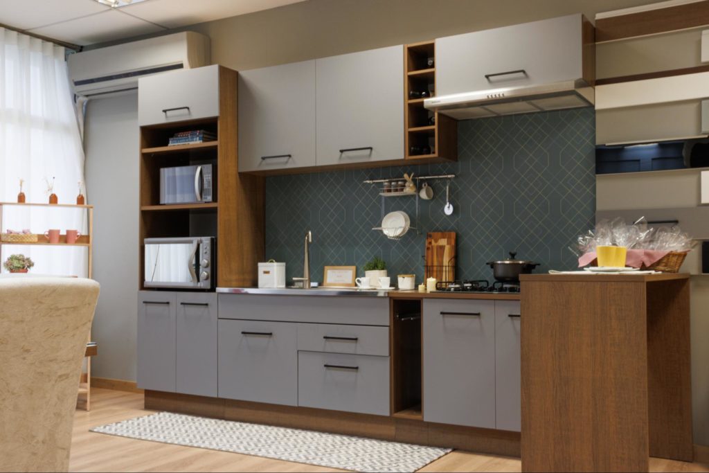 A imagem ilustra um projeto de cozinha Madesa na cor cinza com puxadores pretos e bancadas decoradas com utensílios de cozinha e eletrodomésticos.