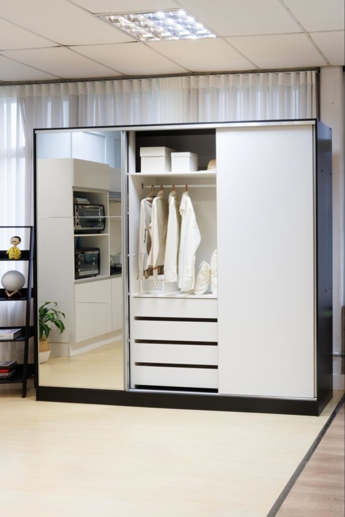 A imagem ilustra um dos modelos de guarda-roupa simples da Madesa com a porta do meio aberta. Essa porta é espelhada e estão à msotra camisas brancas.