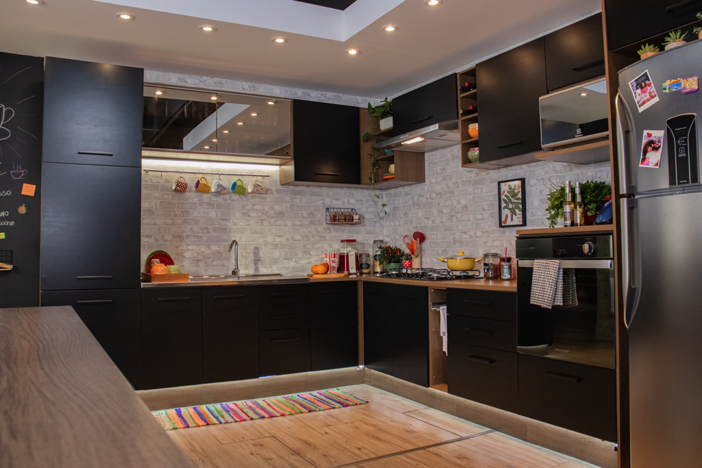 A imagem ilustra um projeto de cozinha planejada Madesa na cor preta, com eletromésticos como geladeira, fogão, microondas e outros acessórios.