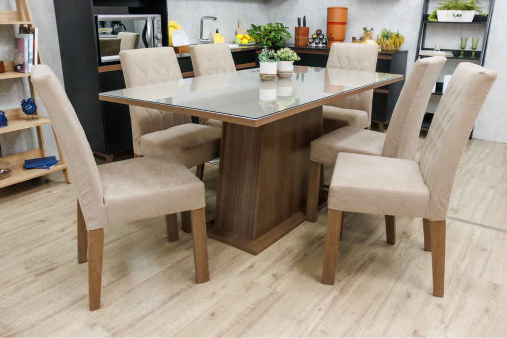 A imagem ilustra uma mesa de jantar de madeira com 6 cadeiras, em cima dela estão dois vasinhos de plantas.