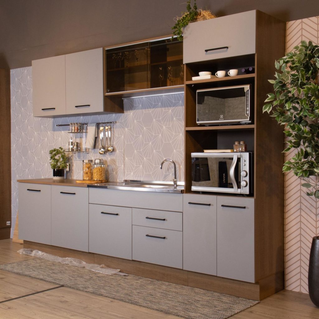 A imagem ilustra o projeto de cozinha Ágata da Madesa, com armários planejados de cor cinza e puxadores pretos em uma cozinha ampla, com plantas e itens decorativos.