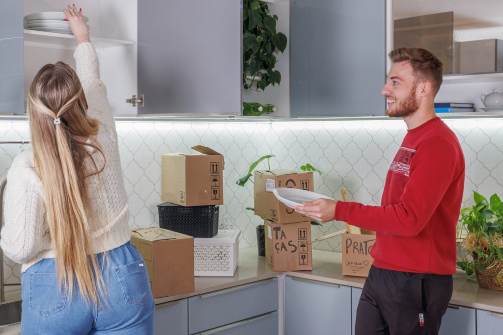 A imagem ilustra um casal em uma cozinha Madesa de cor clara, embalando itens da sua mudança residencial.