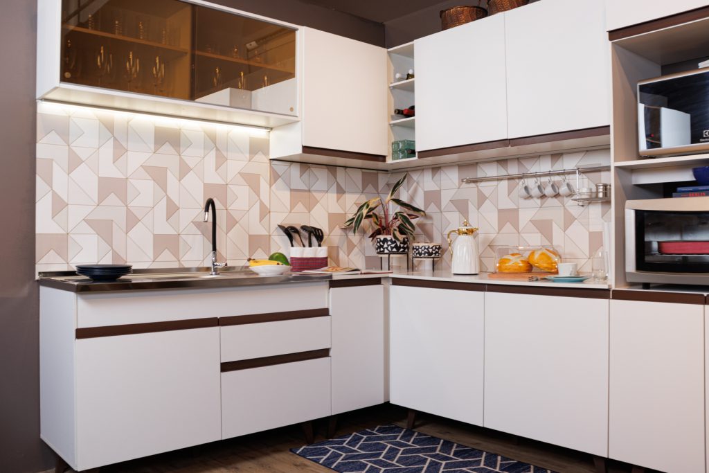 Imagem interna de uma cozinha, com destaque para o armário de cozinha em MDF Madesa. O armário em si tem balcão e parte superior também, em formato L, na cor branca. Alguns detalhes da cozinha, em cores diferentes, fazem o destaque decorativo.