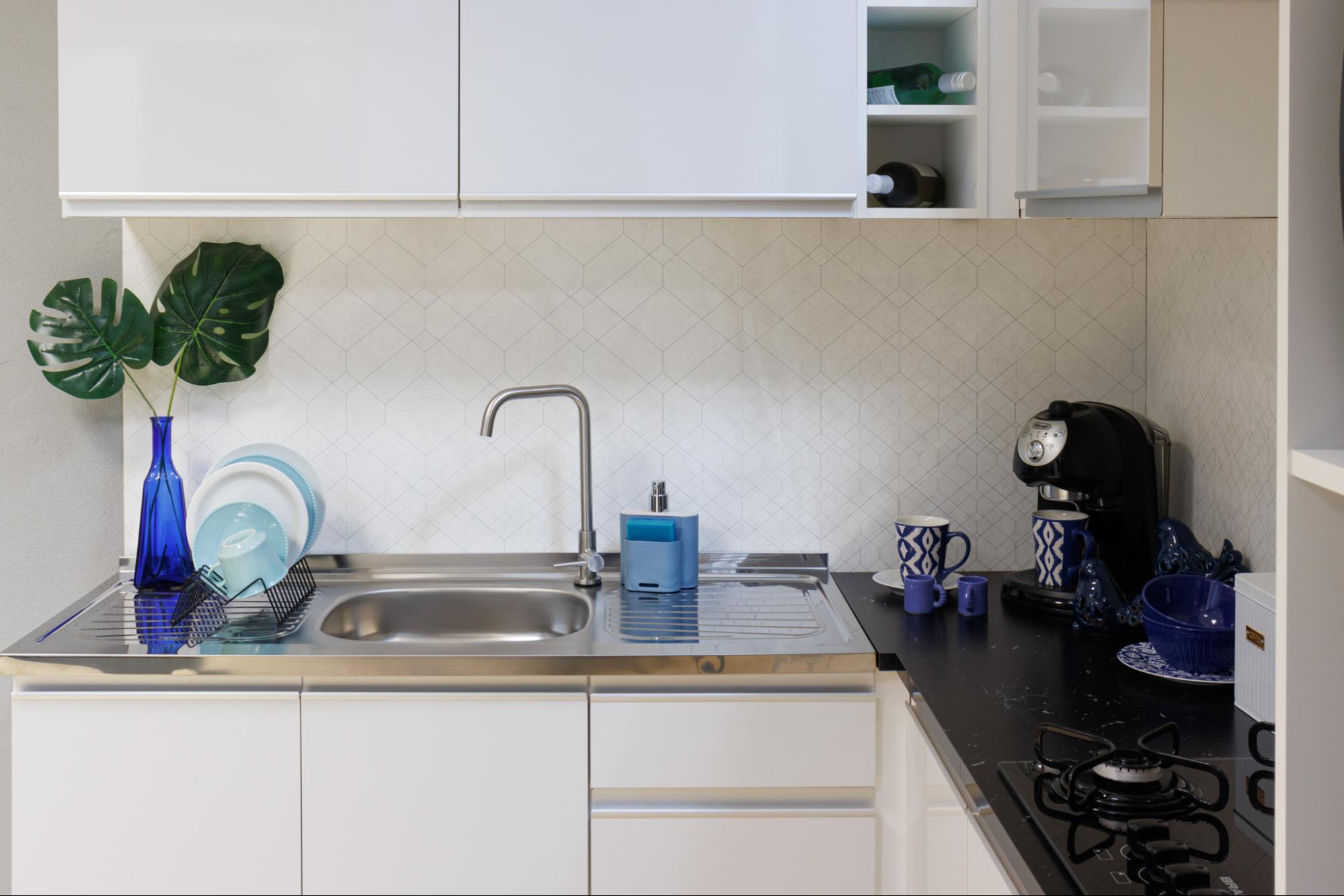 Imagem interna com foco em um armário de cozinha em MDF Madesa, na cor branca. Em modelo L, ele também conta com um vaso de planta de decoração acima da pia