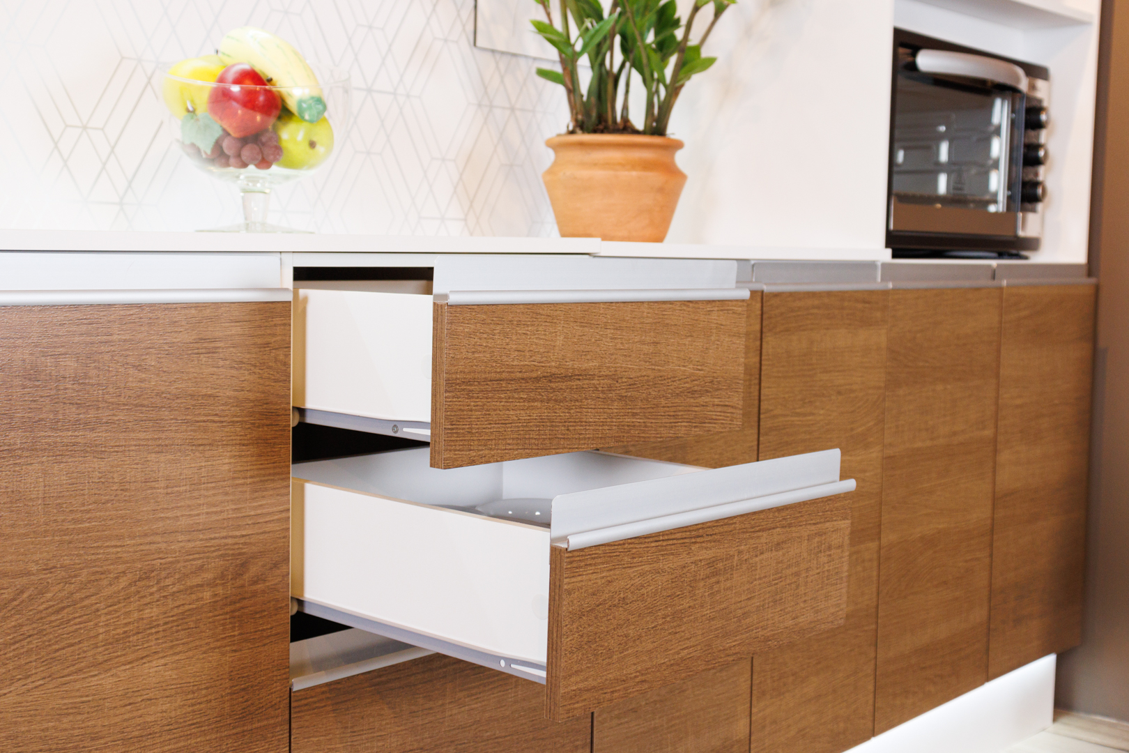 Imagem interna de um armário de cozinha em cor de madeira. Duas das gavetas estão levemente abertas, e em cima do balcão há flores e frutas