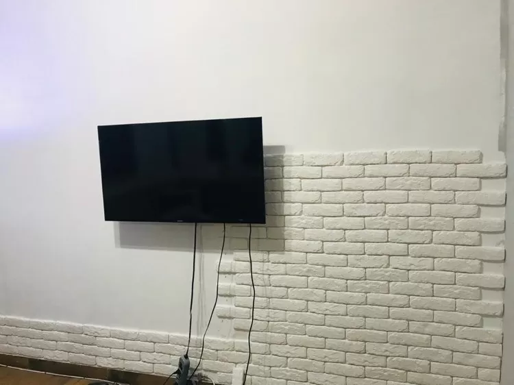 A imagem ilustra uma tv colocada em uma parede de tijolinho branco.