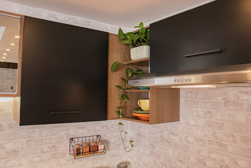 Armário aéreo da cozinha Agata, nas cores preto e rustic, com nichos decorados com plantas e louças.
