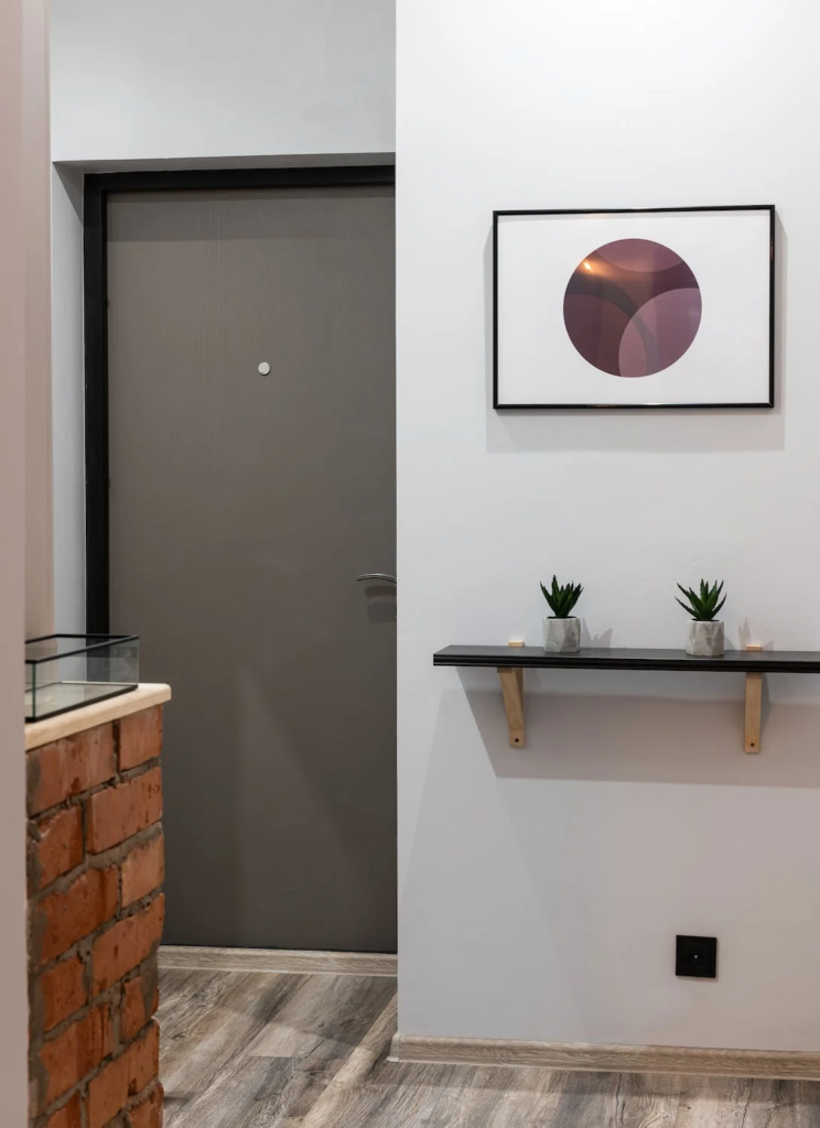 A imagem mostra móveis para hall de entrada em apartamentos pequenos, com uma prateleira com plantinhas e um quadro em formato de círculo.
