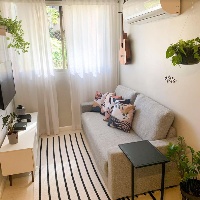 Sala de estar, decorada com uma cortina clara e diversas plantas. À esquerda, um rack Madesa na cor branca.