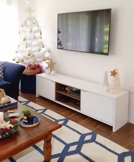 Sala de estar com decoração natalina moderna, com móveis brancos e detalhes em azul e uma árvore de Natal branca com bolinhas douradas.