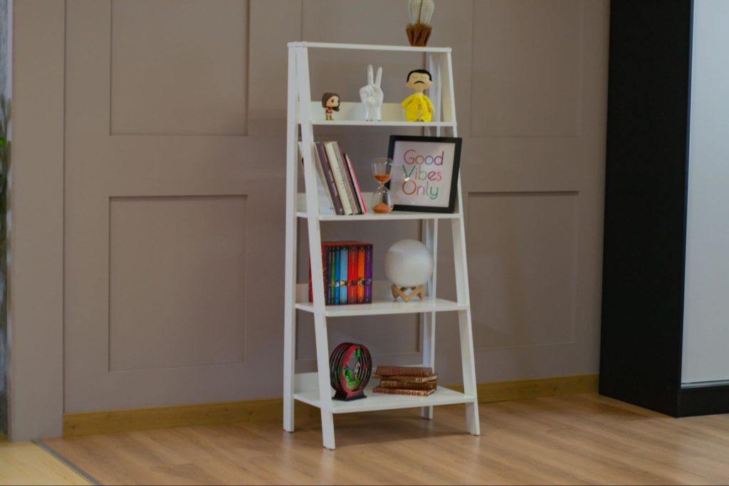A imagem mostra uma estante escada na cor branca com itens decorativos, ilustrando os móveis para hall de entrada.