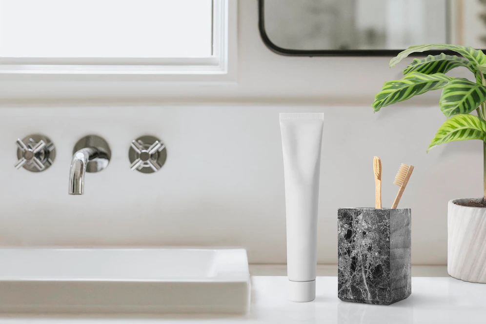 A imagem ilustra o banheiro clean através de uma pia branca e um porta- escovas-de-dente preto com 2 escovas de bambu.