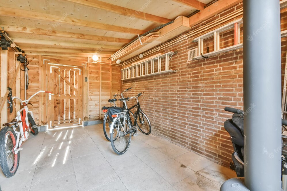 A imagem ilustra uma garagem simples de tijolo à vista com algumas bicicletas e escadas na parede.
