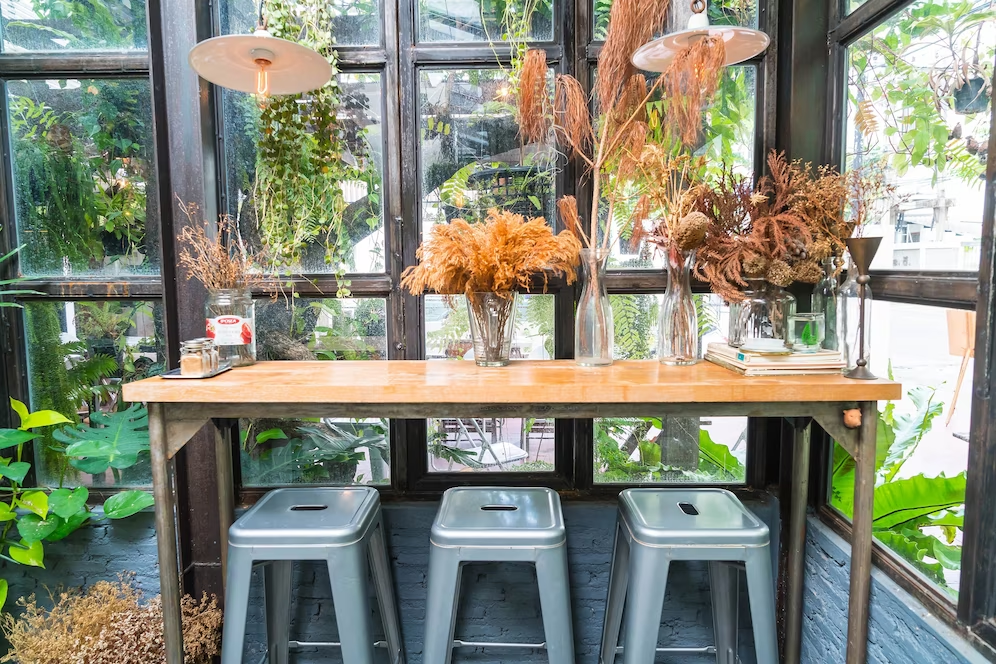 A imagem ilustra um jardim de inverno na sala de jantar, com uma mesa ao centro e um vidro atrás, repleto de plantas.