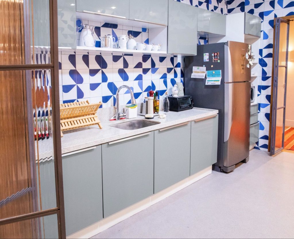 A imagem ilustra a cozinha dos sonhos Madesa, com armários e bancadas de cor cinza claro e uma parede geométrica azul ao fundo.