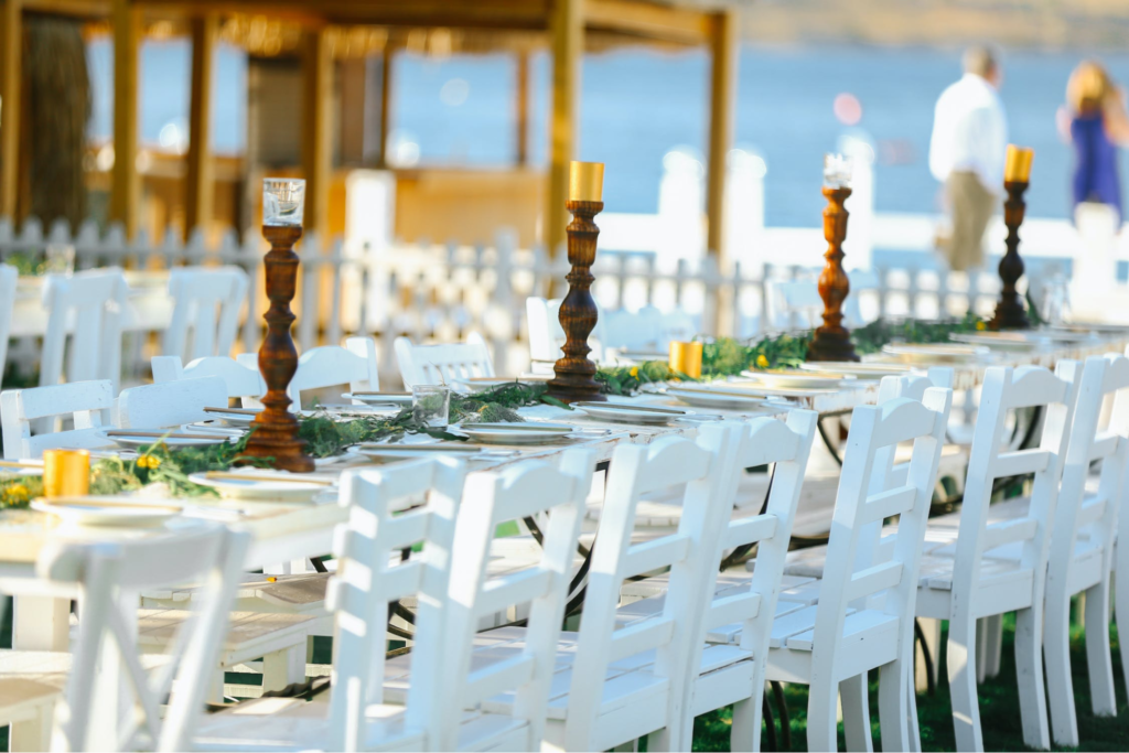 A imagem ilustra cadeiras brancas de madeira compondo a decoração de casamento na praia.