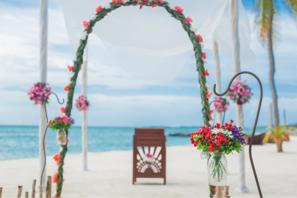 A imagem ilustra uma bela decoração de casamento na praia com flores coloridas em um arco.