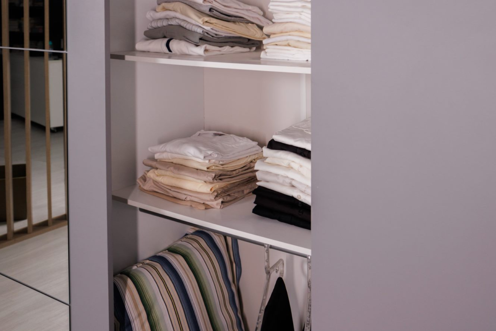A imagem ilustra roupas dobradas em divisórias de um quarto com closet pequeno.