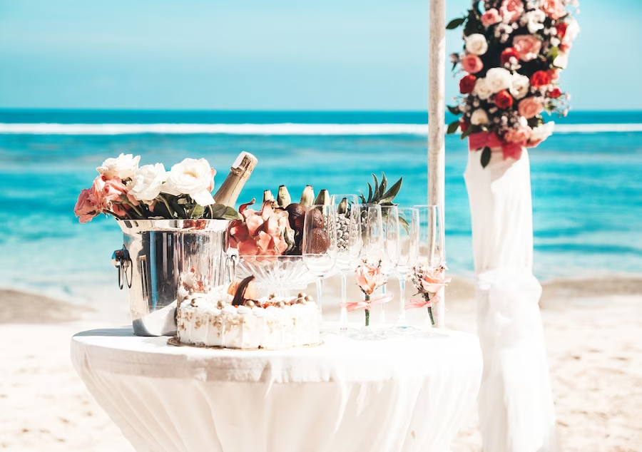 A imagem ilustra uma linda decoração de casamento na praia com flores e uma toalha branca.