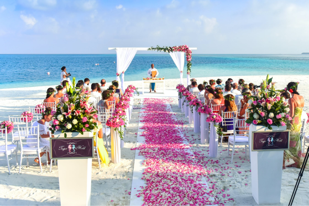 A imagem ilustra uma decoração de casamento na praia que faz do caminho da noiva um caminho com pétalas de rosa.