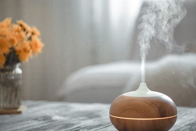 A imagem ilustra um difusor aromático ligado e ao fundo um vaso de flores laranjas, criando um ambiente ideal para a higiene do sono.
