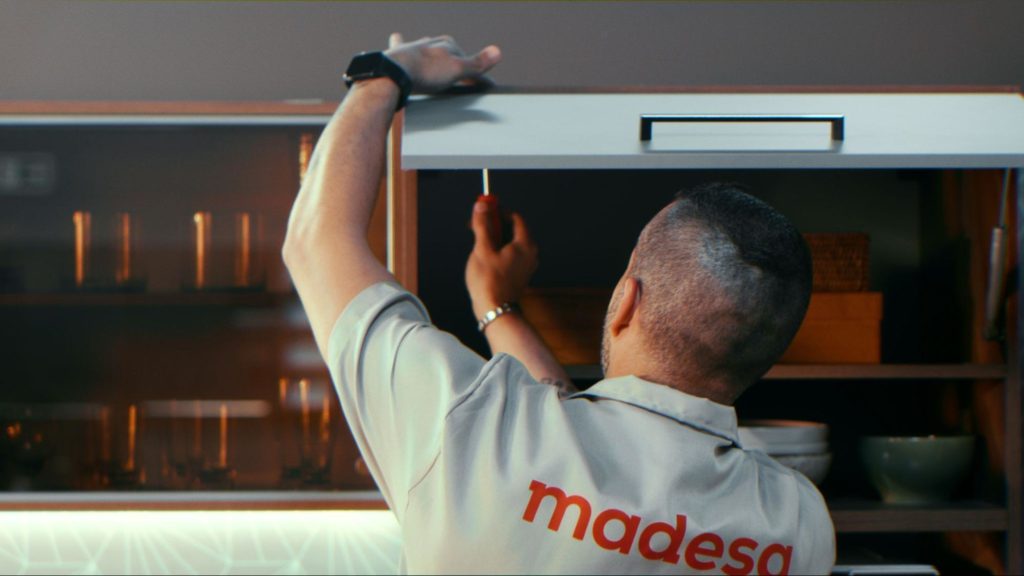 A imagem ilustra um trabalhador Madesa parafusando uma cozinha planejada pequena, simples e barata.