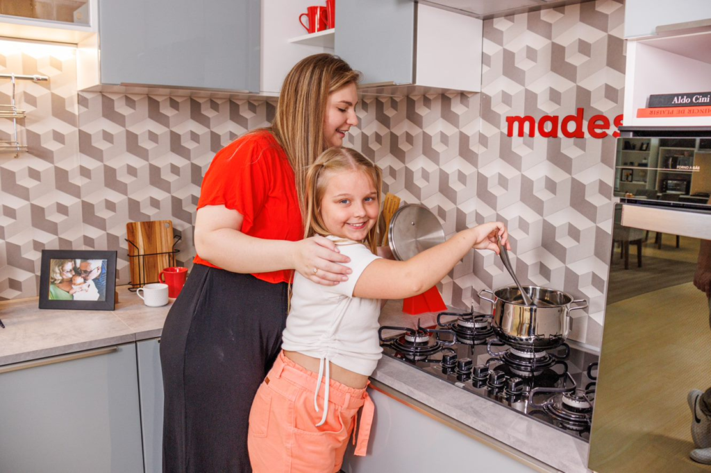 a imagem ilustra uma mãe e uma filha, ambas loiras, em uma cozinha Madesa, dividindo os afazeres domésticos.