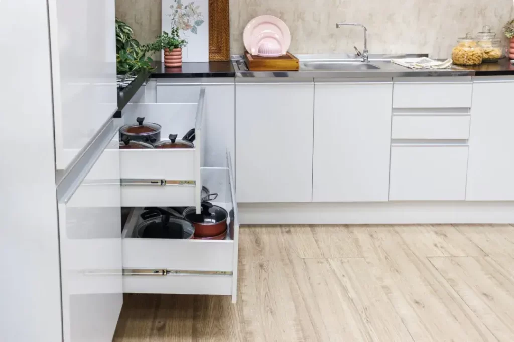 A imagem ilustra um armário de cozinha onde se guarda a lista de utensílios de cozinha com as gavetas abertas.