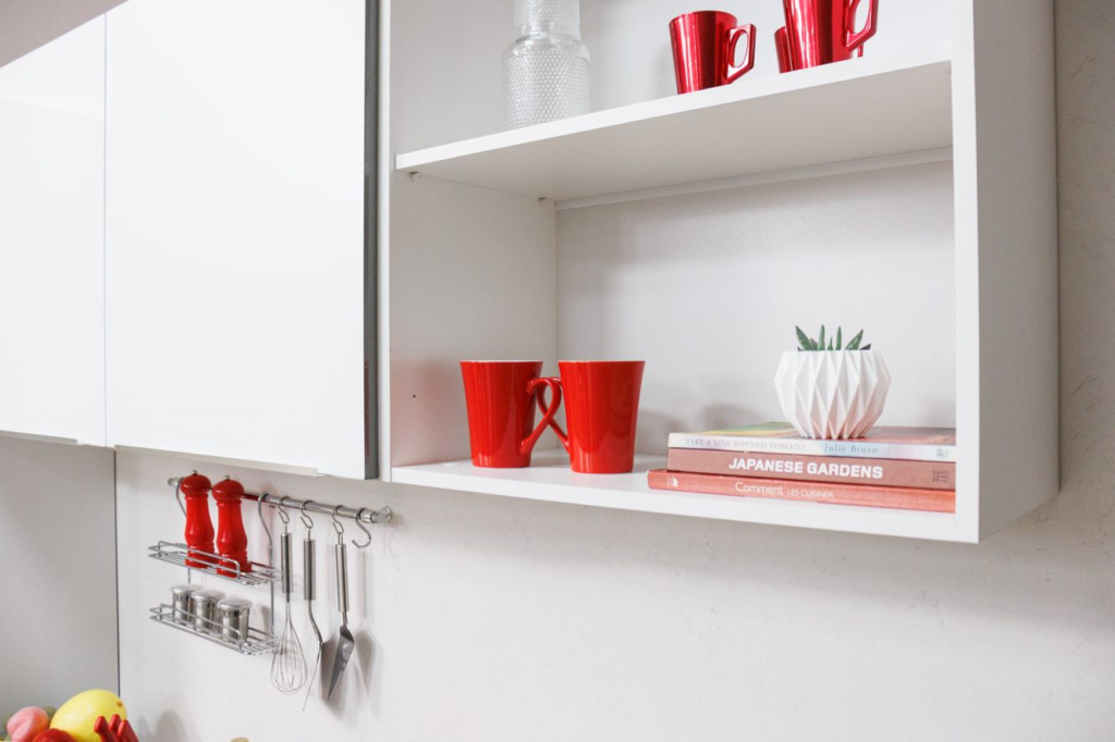 na imagem, alguns objetos de cozinha na cor vermelha estão dispostos  e pendurados em um armário Madesa na cor branca