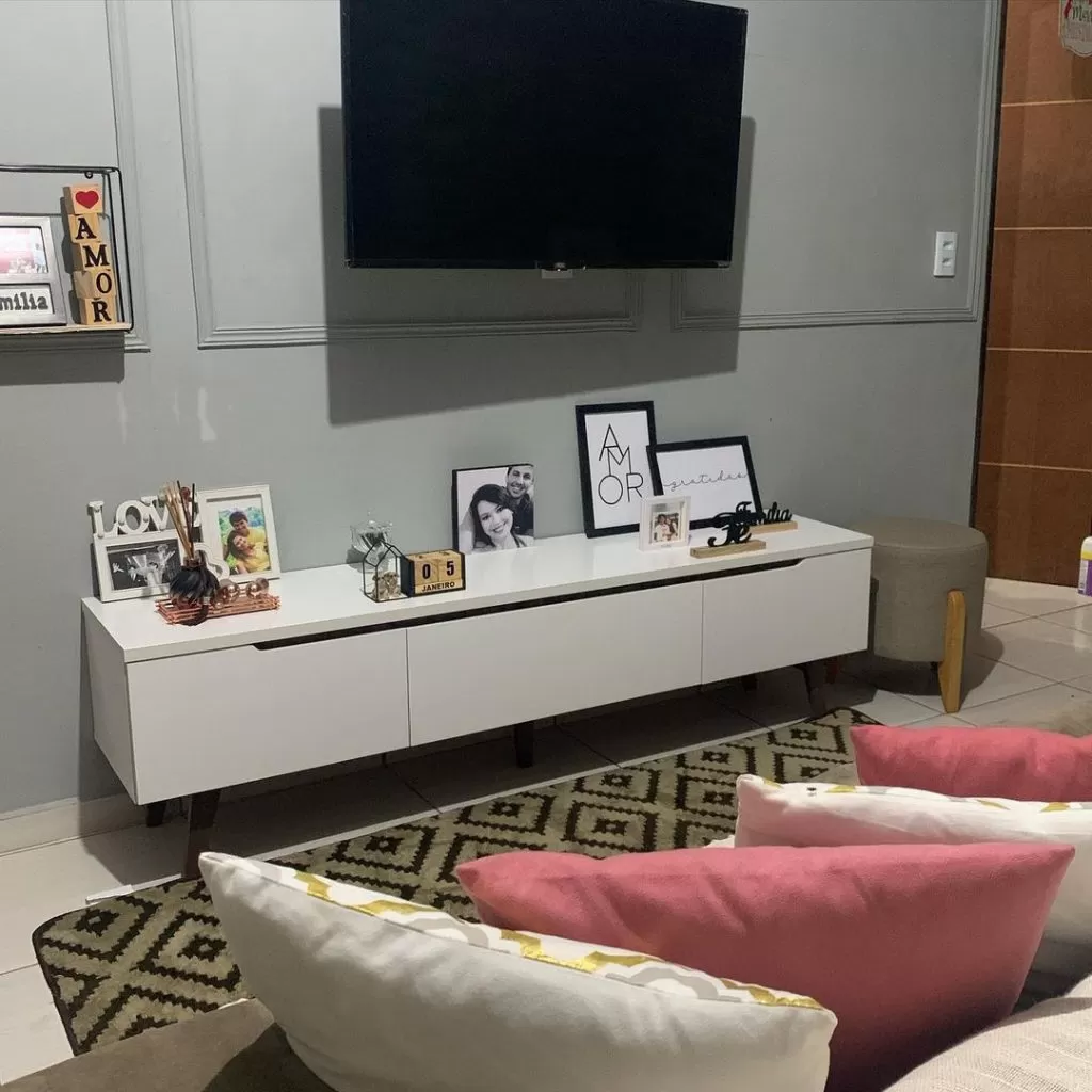Sala de estar decorada com rack Madesa, na cor branca, decorado com diversos quadros de família e frases motivacionais.
