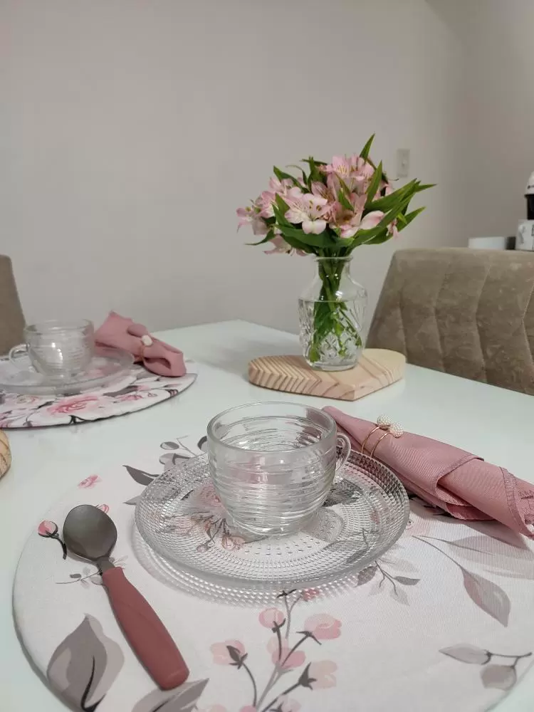 Mesa posta, decorada com xícaras e guardanapos de tecido rosa, estampados com flores também na cor rosa.