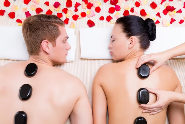 A imagem ilustra um casal deitado de bruços com pedras em suas costas, simbolizando o spa em casal como uma das ideias para o dia namorados.