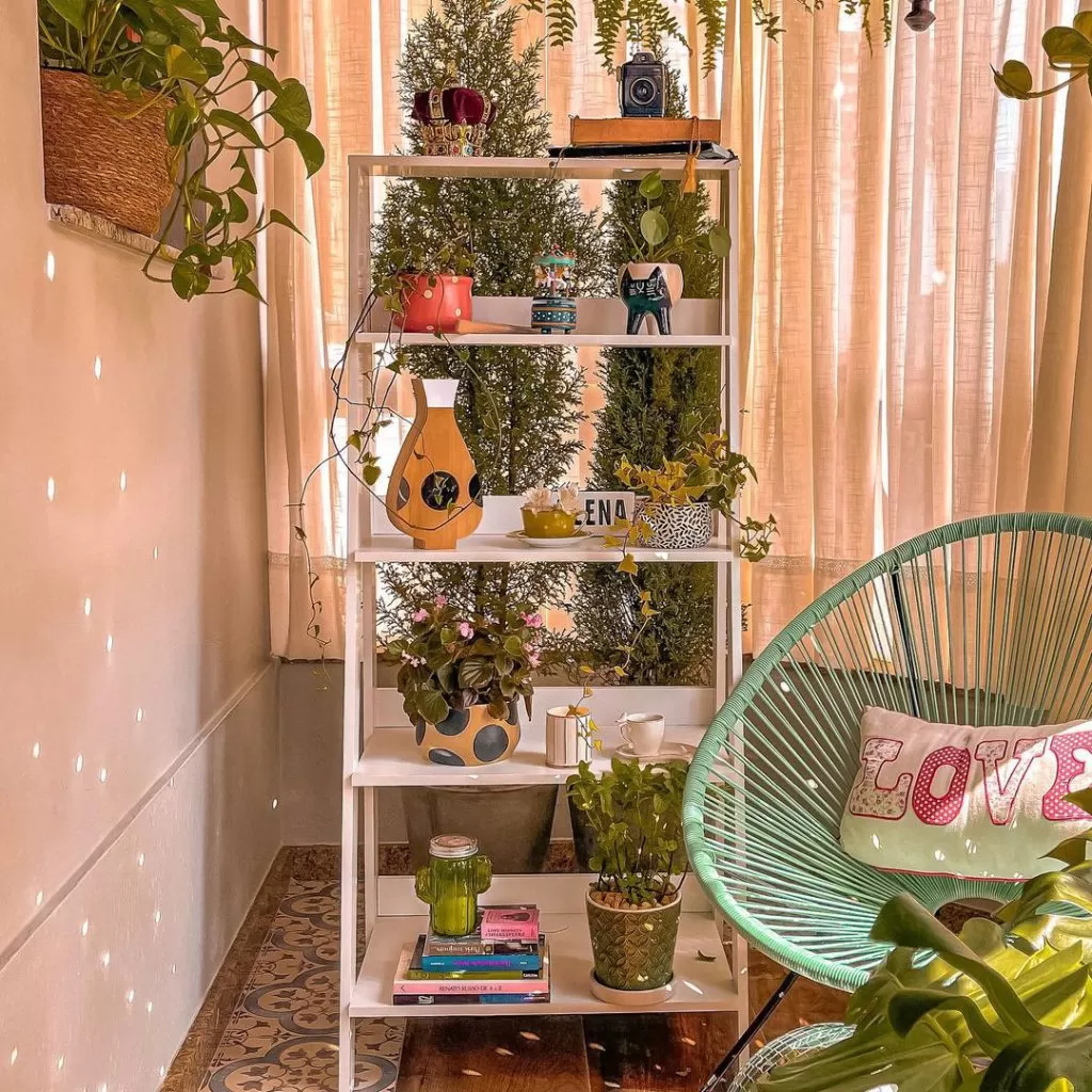 Estante escada Madesa, na cor branca, decorada com diversas plantas em vasos decorados. À direita, uma cadeira com uma almofada escrito “LOVE”.