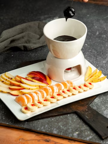 A imagem ilustra uma bandeja branca com frutas para fondue e uma tigela de chocolate.