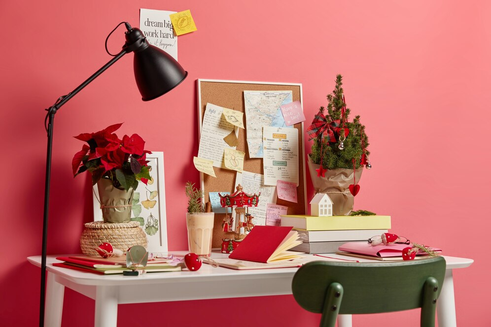 A imagem ilustra um quarto rosa com uma escrivaninha branca. Sobre ela estão alguns objetos emnrulhados com papelão e flores vermelhas, simbolizando ideias de reciclagem para decoração.